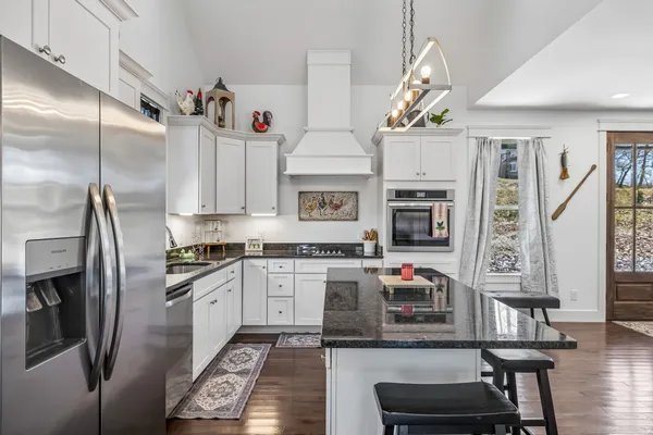 a kitchen with stainless steel appliances granite countertop a refrigerator a stove and a sink with wooden floor