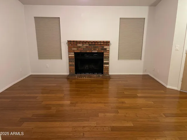 an empty room with wooden floor fireplace and windows