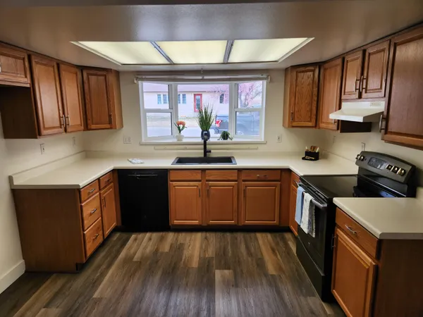 a kitchen with stainless steel appliances granite countertop wooden cabinets a sink a stove a refrigerator and island with wooden floor
