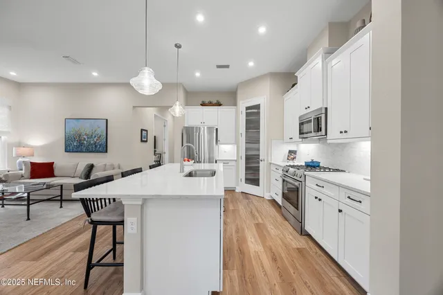 a kitchen with stainless steel appliances kitchen island granite countertop a stove a sink a refrigerator and white cabinets with wooden floor