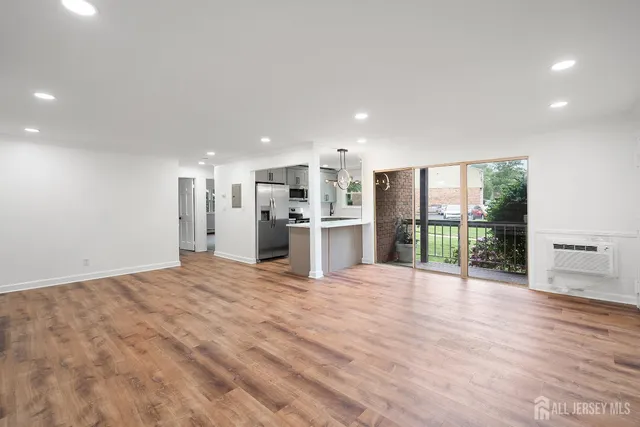 a view of an empty room with wooden floor and a kitchen