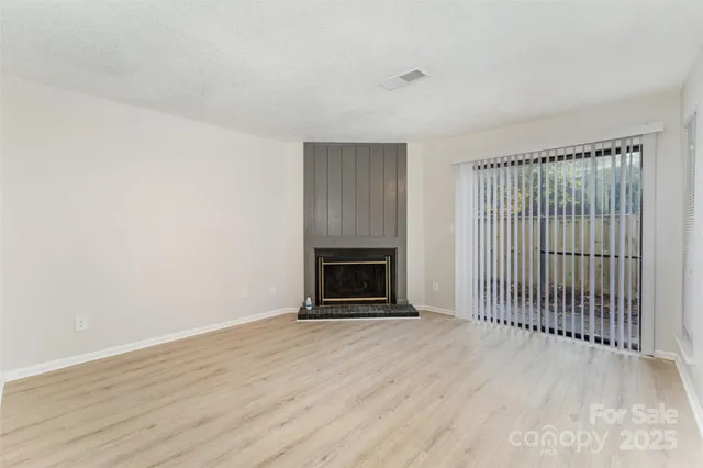 a view of an empty room with wooden floor fireplace and a window
