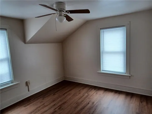 an empty room with wooden floor fan and windows