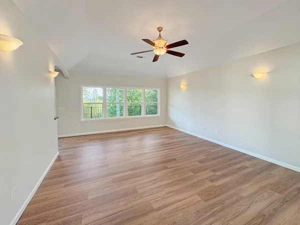 an empty room with wooden floor fan and windows