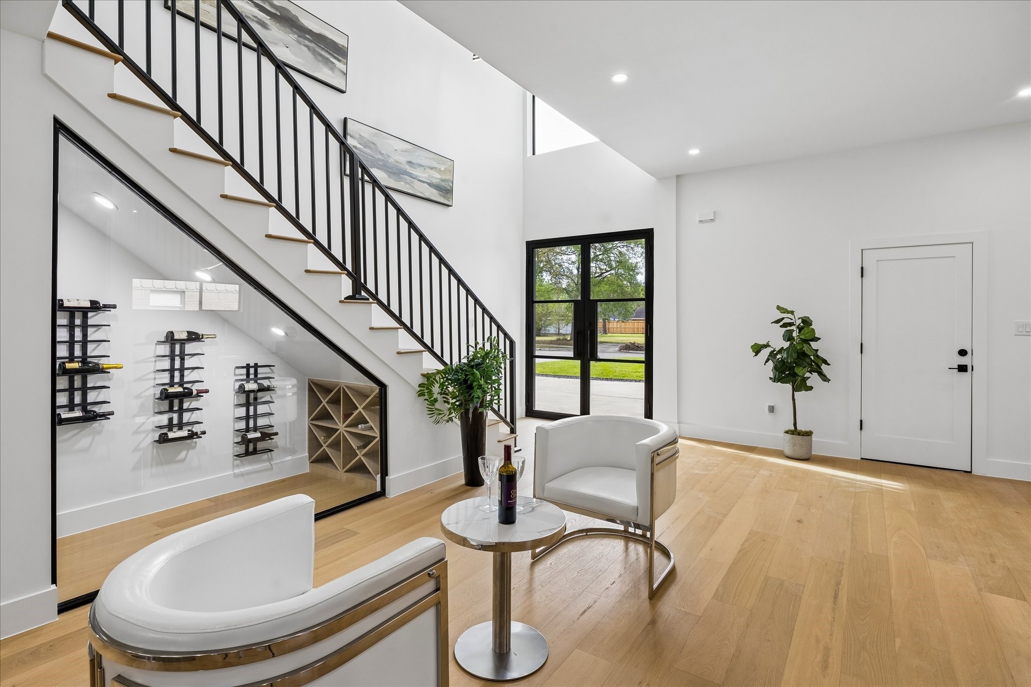 A sleek staircase with a metal railing, a wine storage area under the stairs, and elegant seating. The space is bright and airy, with light wood flooring and contemporary decor.