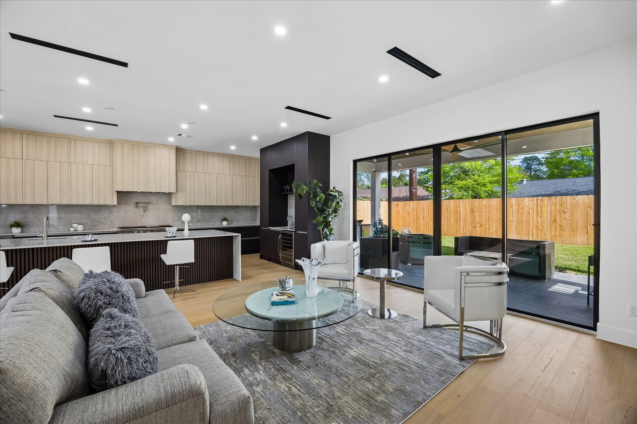5430 Rutherglenn Drive Houston, TX 77096 - Photo 11 of 31 Modern open-concept living space with sleek kitchen, light wood cabinetry, and large sliding glass doors leading to a patio and fenced backyard. Bright and inviting with contemporary furnishings.