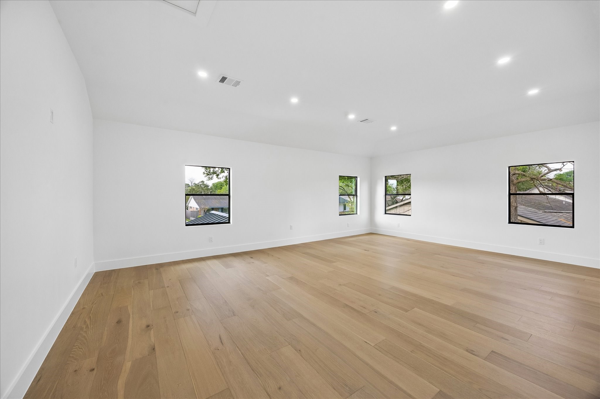 5430 Rutherglenn Drive Houston, TX 77096 - Photo 13 of 31 Spacious, bright room with light wood flooring, white walls, recessed lighting, and multiple windows offering natural light and views of greenery outside. Ideal for a living area or large bedroom.