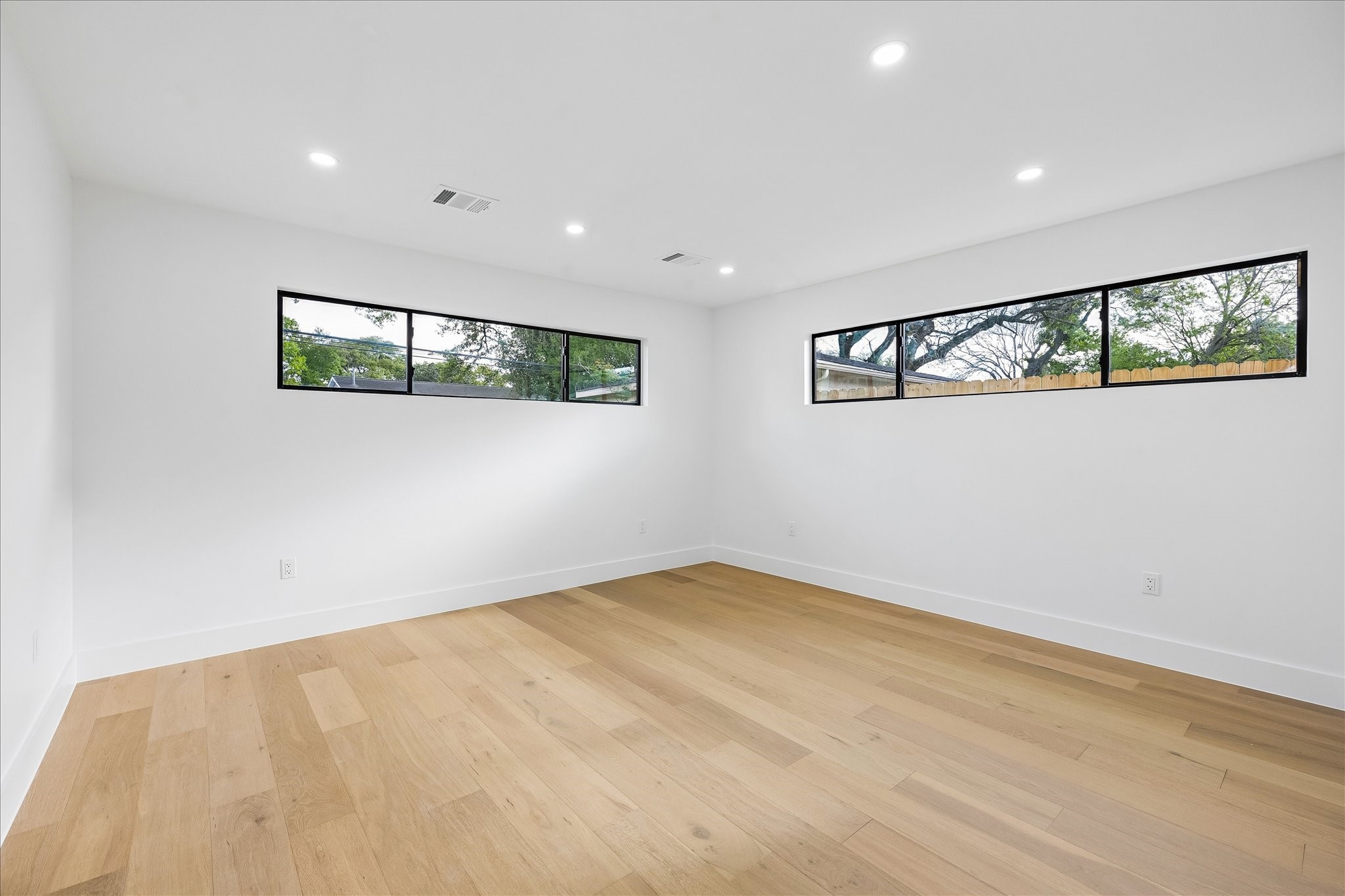5430 Rutherglenn Drive Houston, TX 77096 - Photo 14 of 31 This room features a modern, minimalist design with light wood flooring and two horizontal windows offering ample natural light. The white walls and recessed lighting create a bright and airy atmosphere.