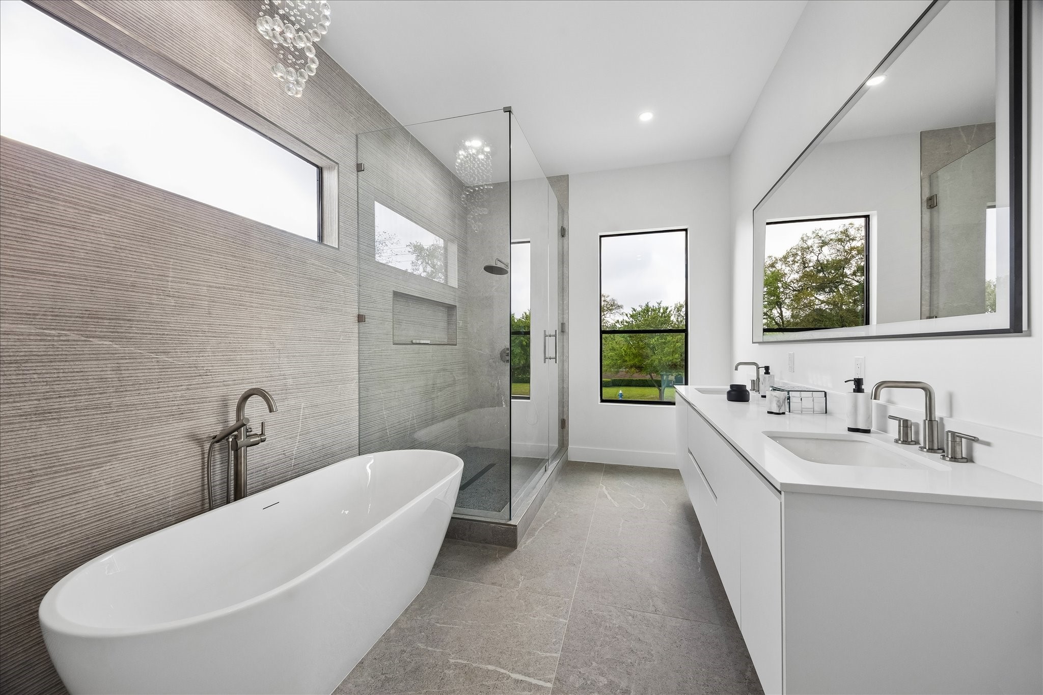 5430 Rutherglenn Drive Houston, TX 77096 - Photo 16 of 31 This modern bathroom features a sleek freestanding tub, a spacious glass-enclosed shower, and a double-sink vanity. Large windows provide ample natural light, enhancing the clean, minimalist design.