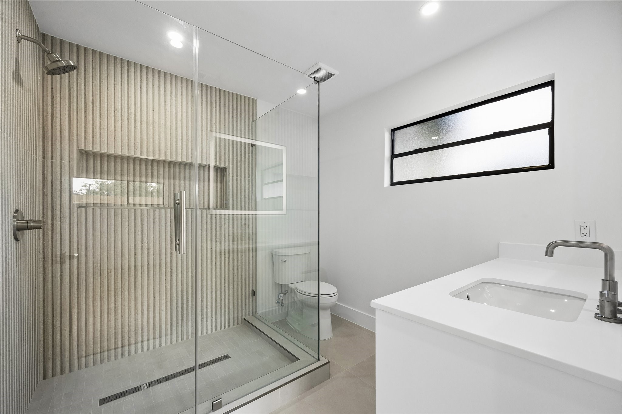 5430 Rutherglenn Drive Houston, TX 77096 - Photo 20 of 31 First floor bathroom features a spacious glass-enclosed shower with textured wall tiles, a sleek vanity with an integrated sink, and a frosted window for natural light.