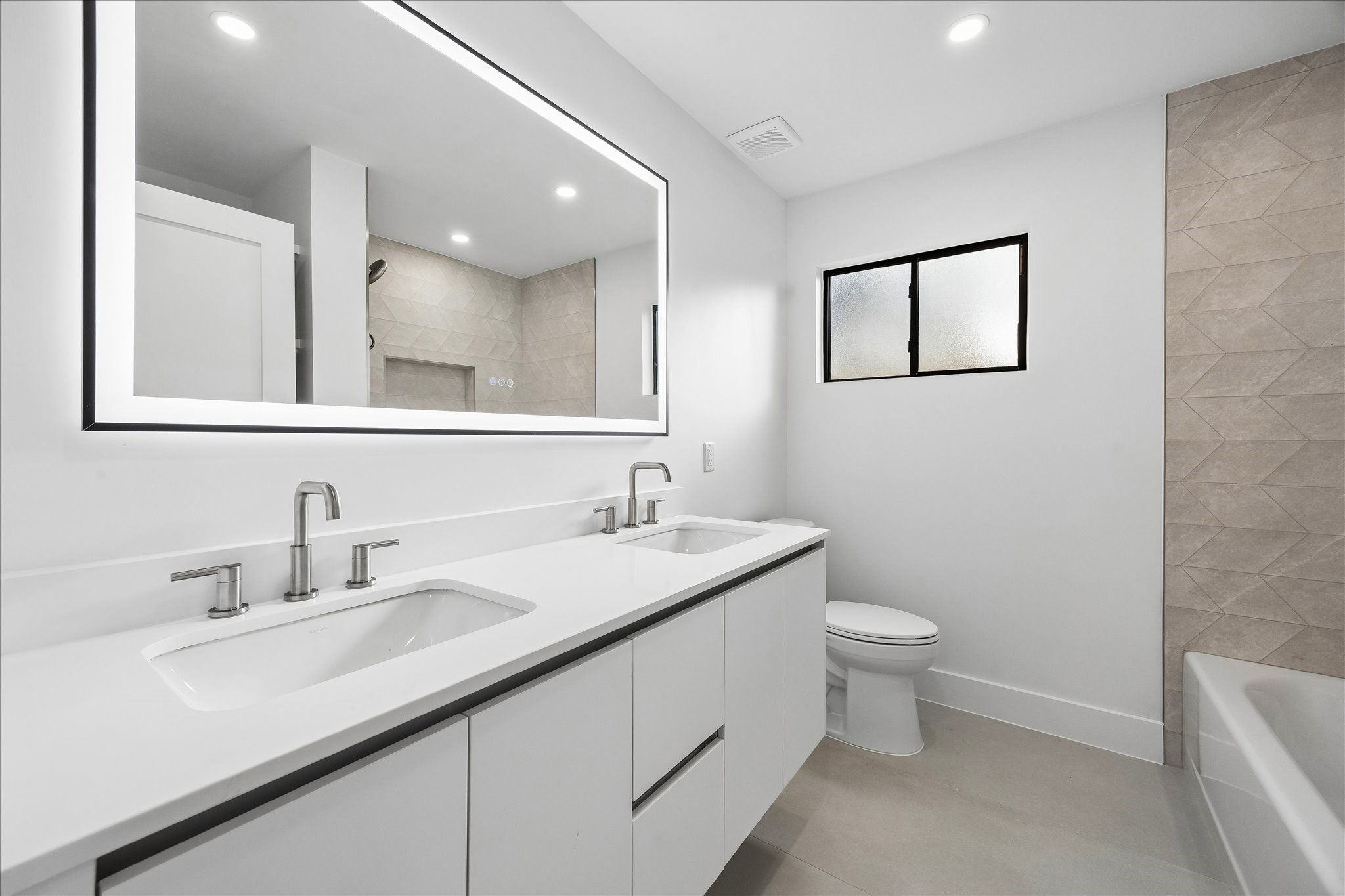 5430 Rutherglenn Drive Houston, TX 77096 - Photo 21 of 31 Another first floor bathroom featuring a dual-sink vanity with sleek faucets, large illuminated mirror, and stylish tiled walls. The space is bright and airy, with a frosted window for privacy.