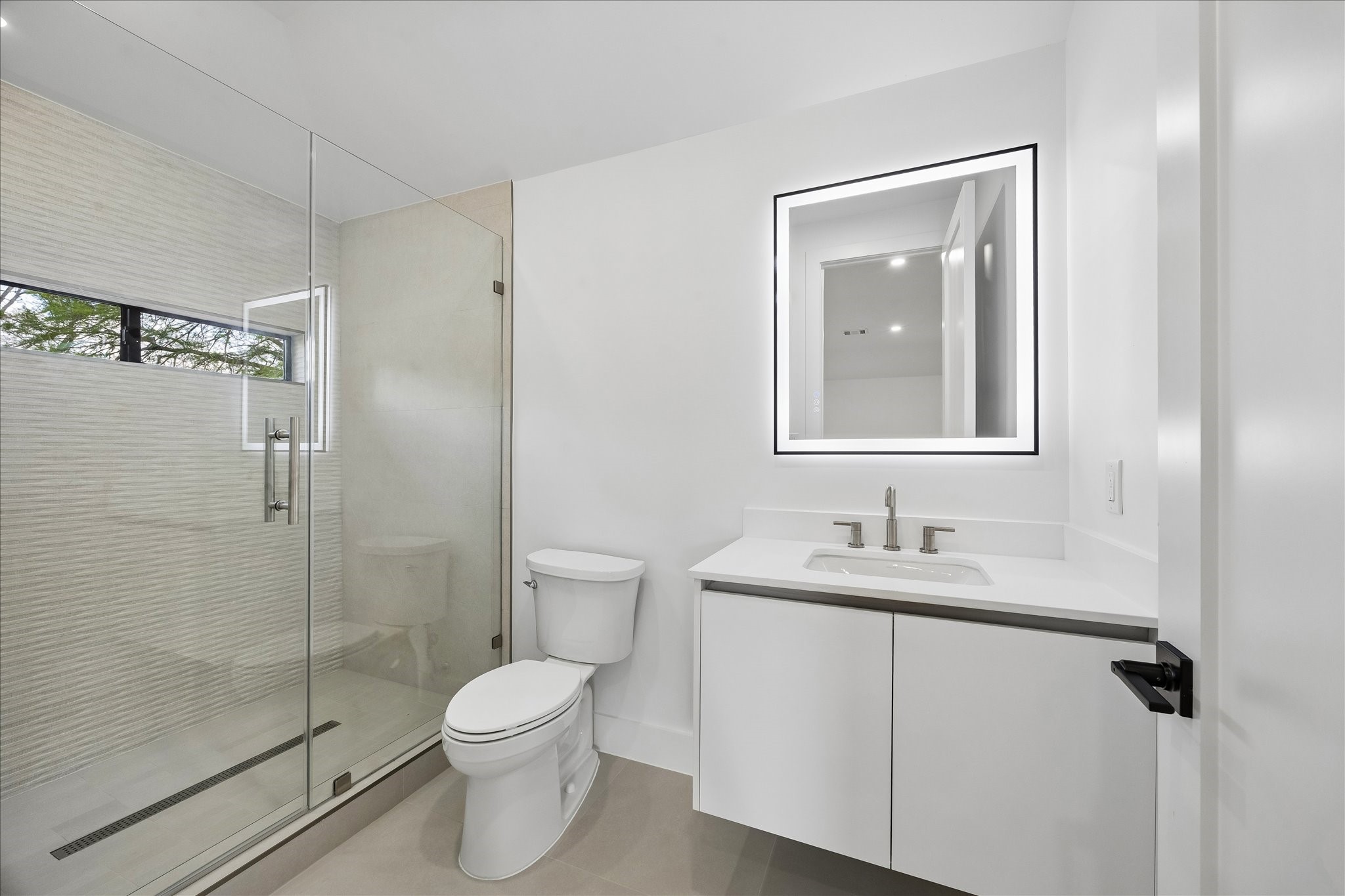 5430 Rutherglenn Drive Houston, TX 77096 - Photo 22 of 31 This bathroom features a modern design with a glass-enclosed shower, sleek vanity with an illuminated mirror, and a neutral color palette for a clean and bright feel.