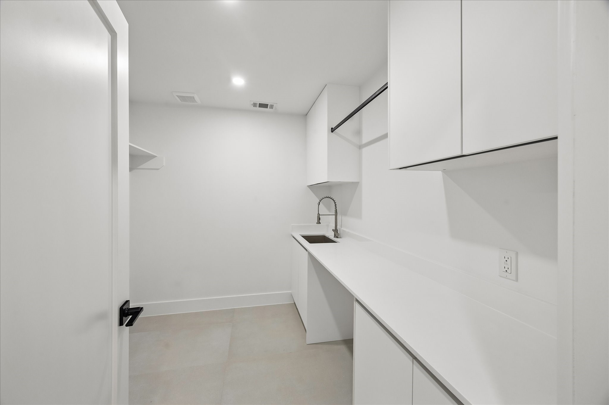 5430 Rutherglenn Drive Houston, TX 77096 - Photo 23 of 31 This photo shows a sleek, modern laundry room with ample white cabinetry, a long countertop, and a built-in sink. The space is well-lit and features minimalist design elements and practicality for hanging clothes.