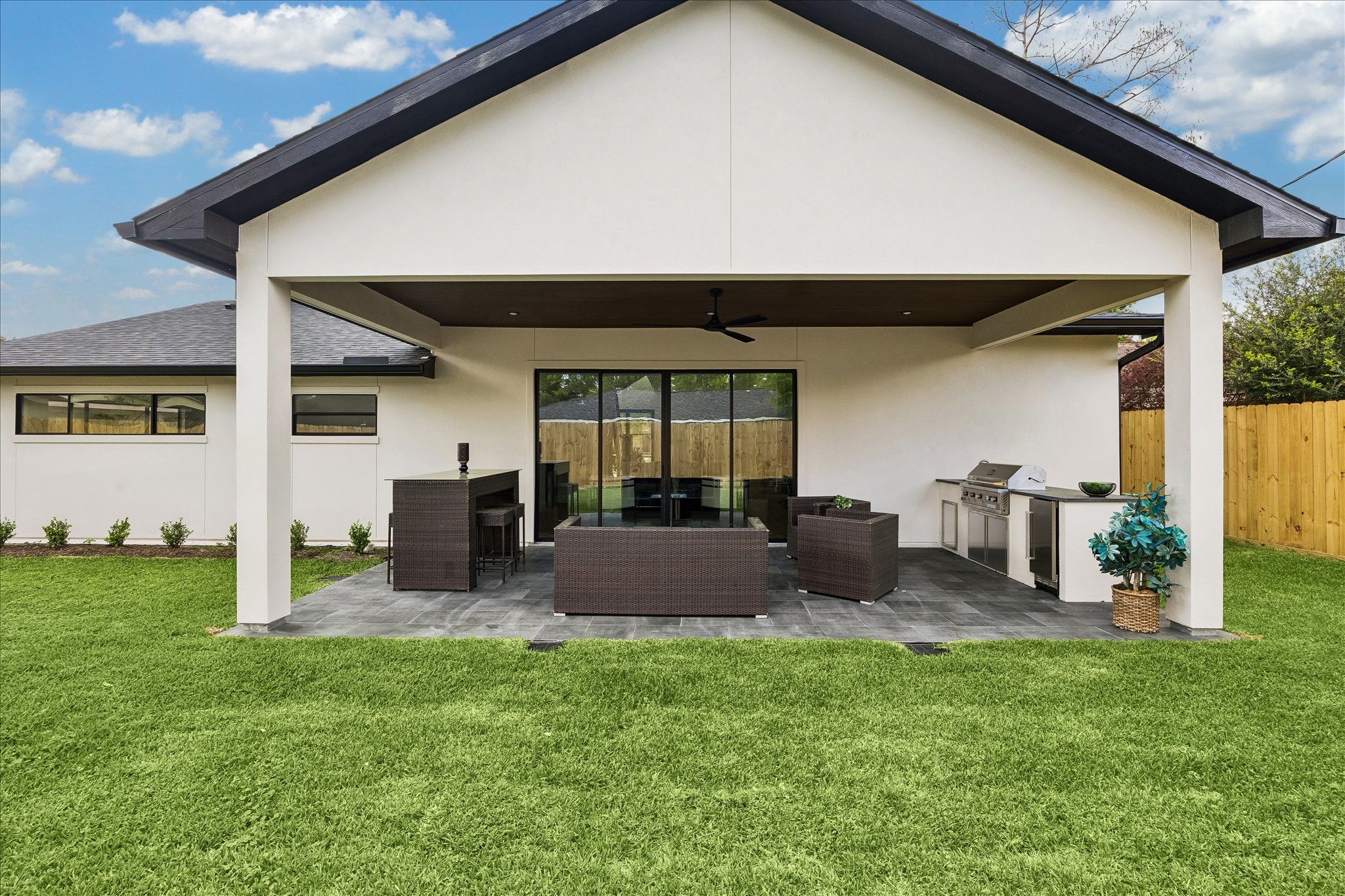 5430 Rutherglenn Drive Houston, TX 77096 - Photo 26 of 31 Large covered patio with sleek outdoor furniture, a built-in grill, and a ceiling fan, set against a well-maintained lawn and a fenced backyard. Ideal for outdoor entertaining.