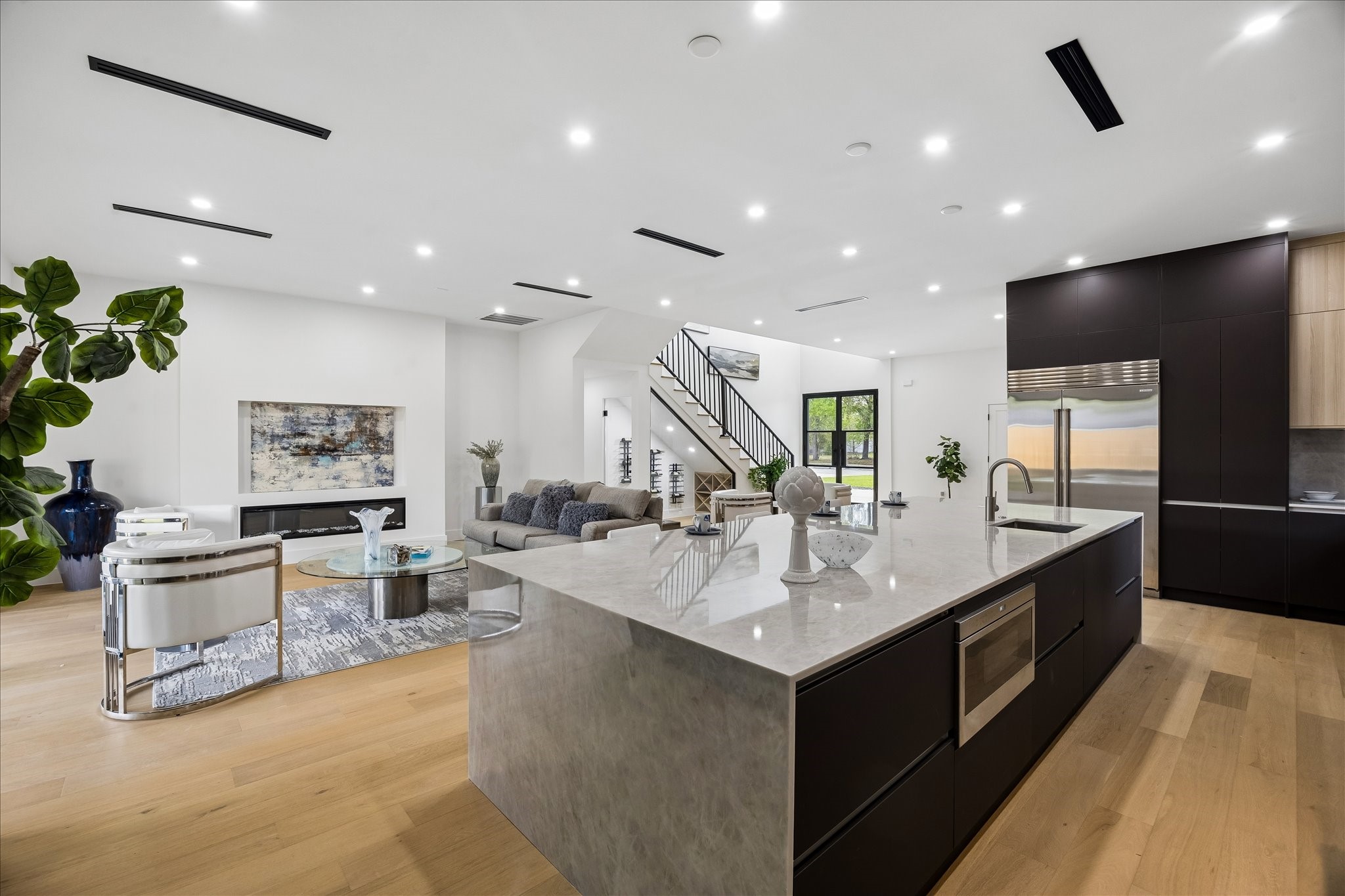 5430 Rutherglenn Drive Houston, TX 77096 - Photo 3 of 31 Modern open-concept living space features a sleek kitchen with a large island, ample seating area, and elegant lighting. The space is bright with hardwood floors and stylish decor, offering a perfect blend of functionality and sophistication.