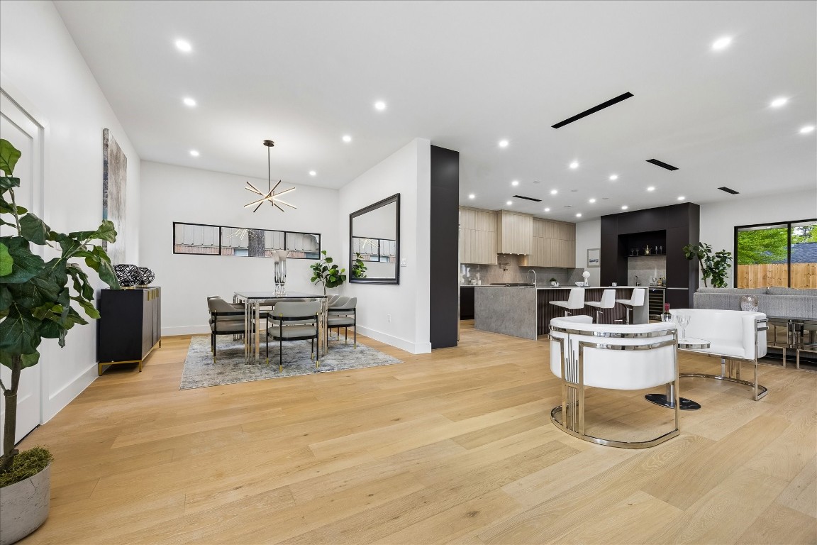 5430 Rutherglenn Drive Houston, TX 77096 - Photo 4 of 31 Lighting galore with a seamless blend of dining and kitchen areas with sleek finishes. The room is well-lit with recessed lighting and a contemporary chandelier, complemented by light wood flooring and stylish furniture. Large windows provide ample natural light and views of a fenced backyard.