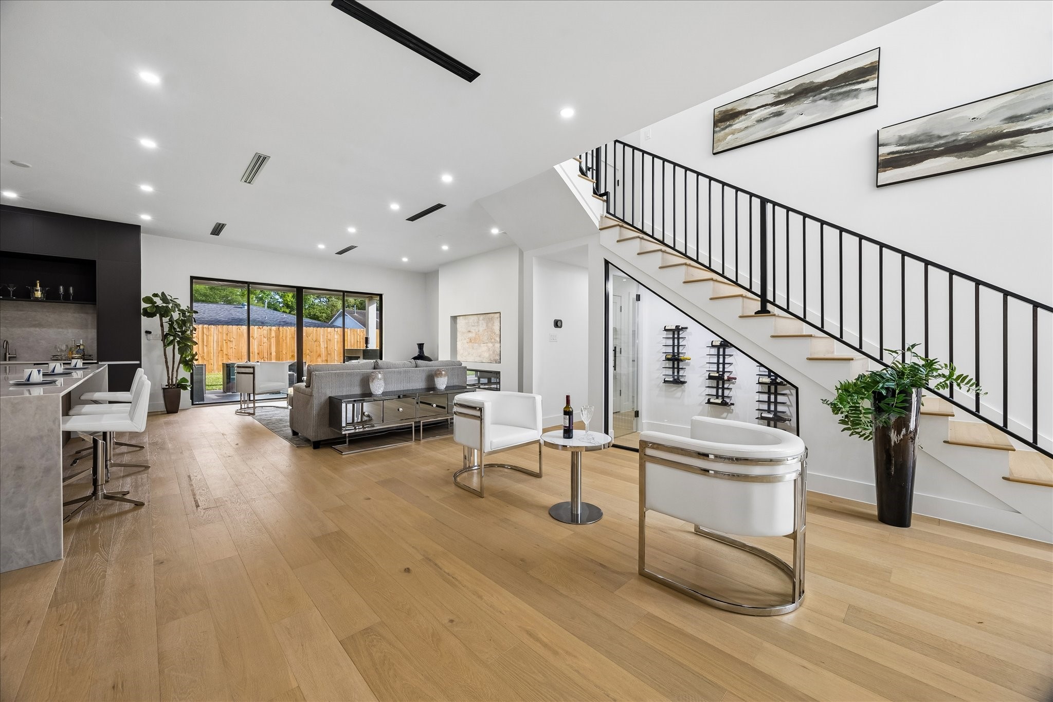 5430 Rutherglenn Drive Houston, TX 77096 - Photo 31 of 31 This spacious, modern living area features an open floor plan with a sleek kitchen, stylish bar seating, and expansive glass doors leading to the backyard. The room is bright and airy, with wood flooring and a contemporary staircase accentuating the space.
