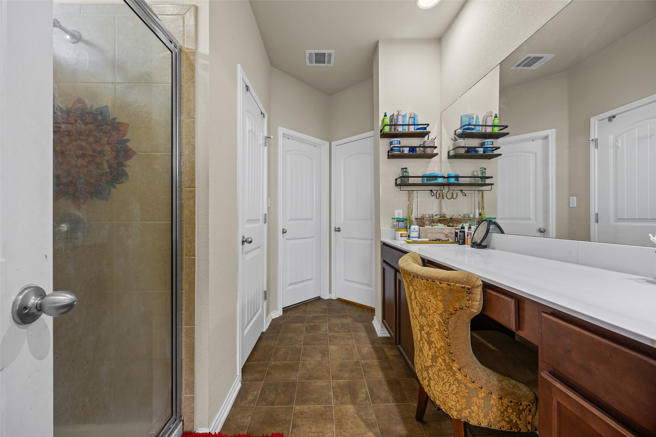 19113 Rookery Trail Pflugerville, TX 78660 - Photo 19 of 36 Bathroom featuring a walk-in shower with glass enclosure, brown tile flooring, long vanity with white countertop, and dark wood cabinetry