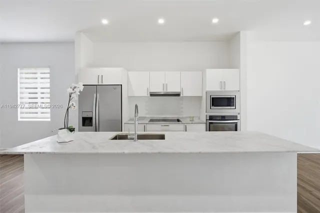 a kitchen with stainless steel appliances a sink a stove a microwave a refrigerator and white cabinets