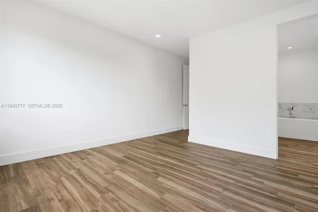 a view of an empty room with wooden floor and a bathroom