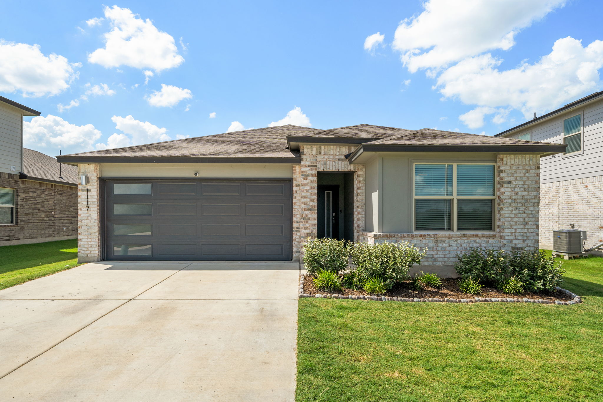 1117 Tipton Street Georgetown, TX 78633 - Photo 2 of 40 Single-story residence featuring a brick and stucco facade, a two-car garage with frosted glass inserts, and a landscaped front yard with established plantings