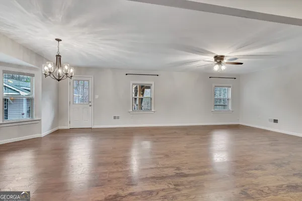 an empty room with a chandelier fan and windows