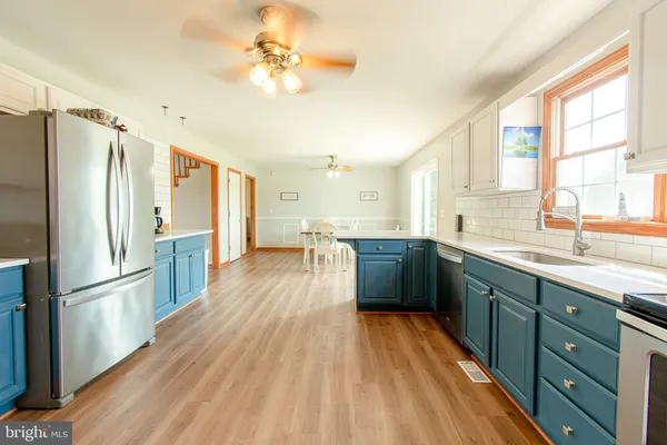 a kitchen with stainless steel appliances a refrigerator a sink dishwasher a stove and white countertops with wooden floor