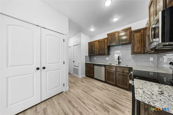 a kitchen with stainless steel appliances granite countertop a refrigerator a sink dishwasher and wooden cabinets with wooden floor