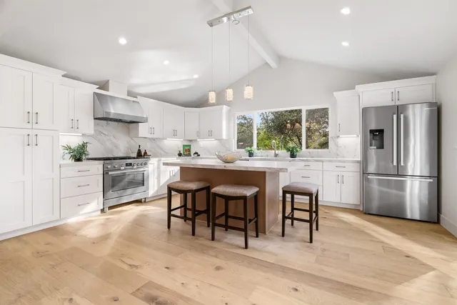 a kitchen with stainless steel appliances granite countertop a stove a sink a refrigerator a dining table and chairs