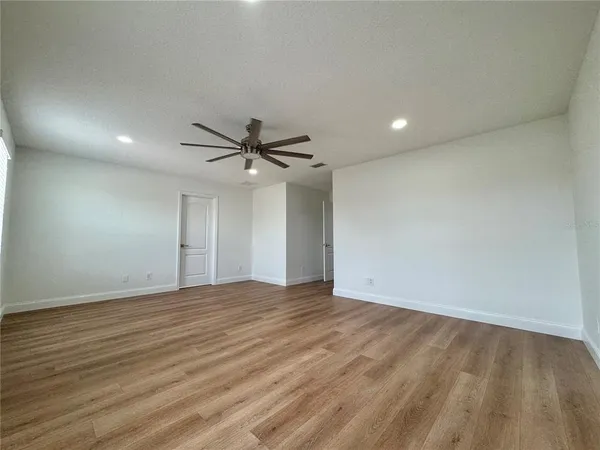 a view of an empty room with wooden floor and a ceiling fan
