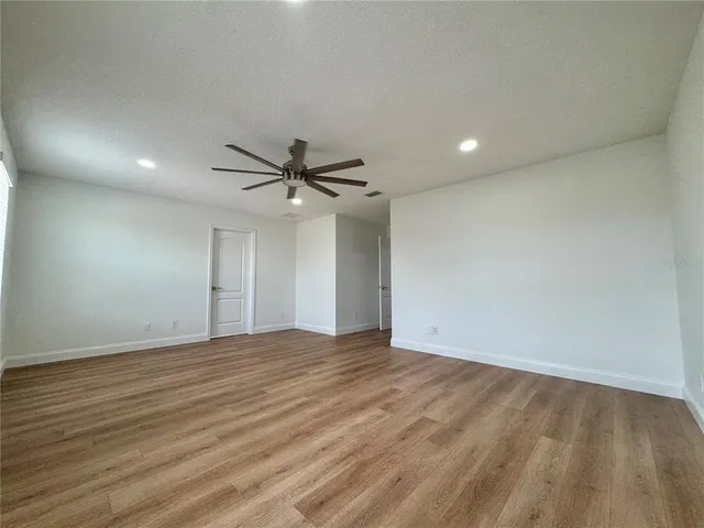 a view of an empty room with wooden floor and a ceiling fan