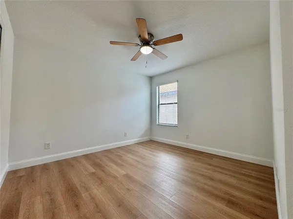 an empty room with wooden floor ceiling fan and windows