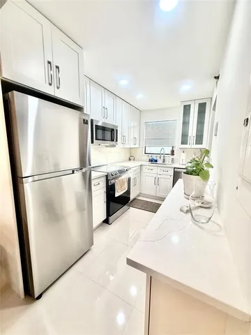 a kitchen with stainless steel appliances granite countertop a refrigerator a stove a sink a microwave a refrigerator and white cabinets with wooden floor