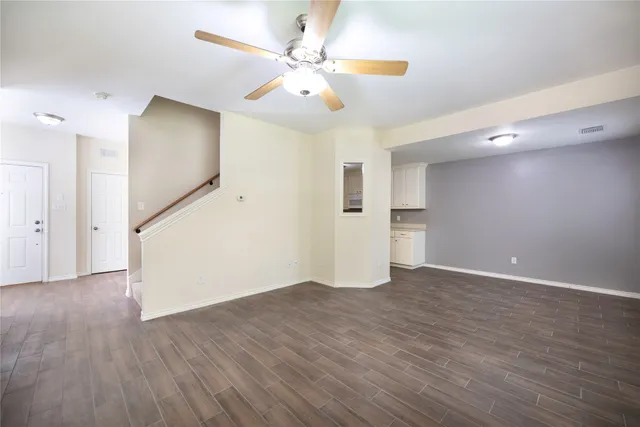 a view of an empty room with wooden floor and a ceiling fan