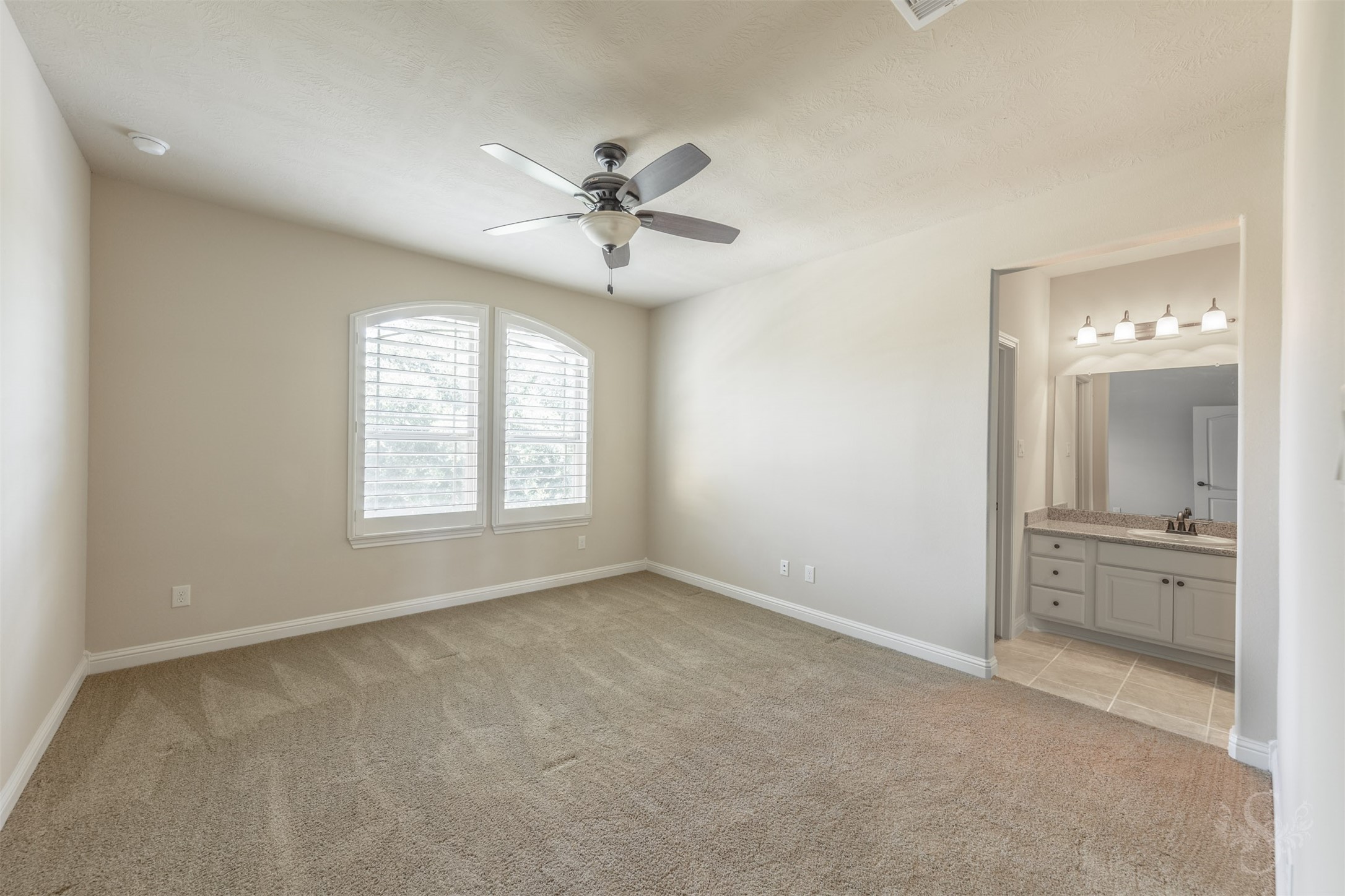 5803 Mustang Ridge Lane Fulshear, TX 77441 - Photo 29 of 48 Spacious secondary bedroom offers a quiet retreat with arched windows featuring plantation shutters and direct access to a private en-suite bath. Neutral finishes and generous proportions create a comfortable, inviting atmosphere.