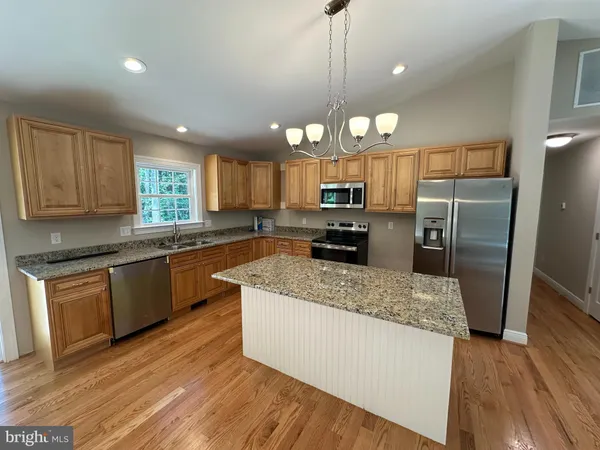 a large kitchen with a center island wooden floor stainless steel appliances and cabinets