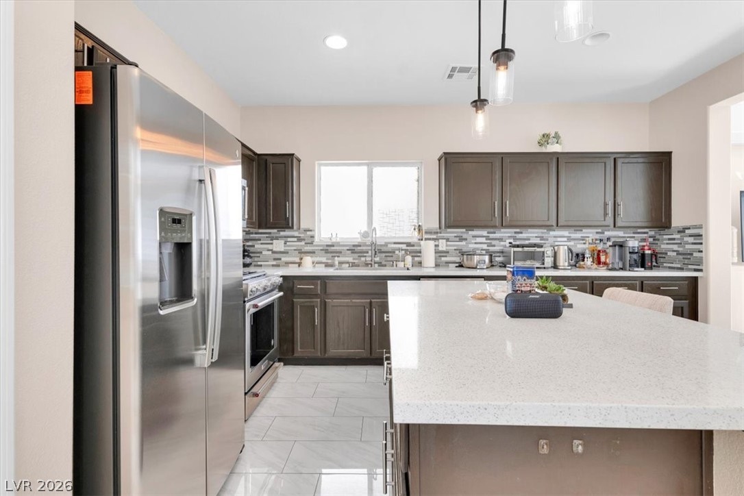 1019 Garnet Ridge Court Las Vegas, NV 89123 - Photo 5 of 34 Kitchen featuring stainless steel appliances, dark wood finish cabinetry, a center island, decorative light fixtures, and light stone countertops