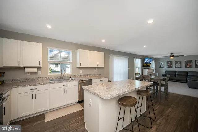 a open kitchen with granite countertop a stove a sink a dining table and chairs with wooden floor