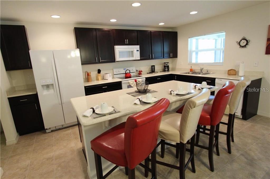 957 Emerald Green Court Kissimmee, FL 34746 - Photo 10 of 29 a kitchen with stainless steel appliances kitchen island granite countertop a table chairs sink and microwave
