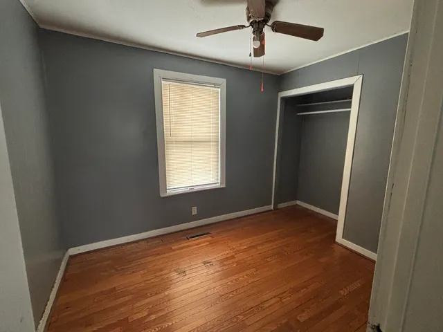 an empty room with wooden floor ceiling fan and windows