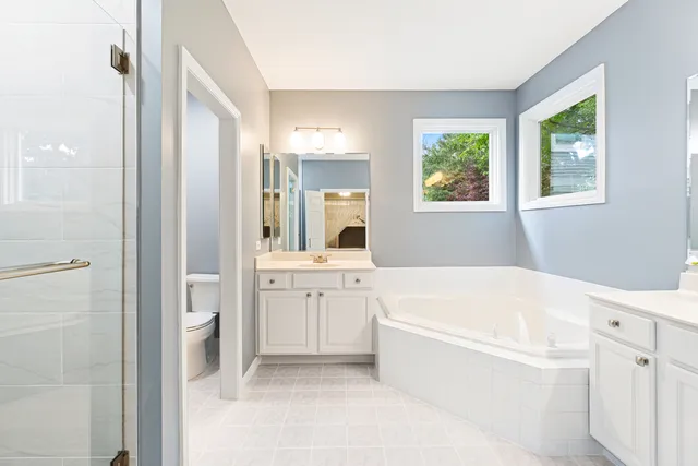 a bathroom with a bathtub a double vanity sink a window and a mirror