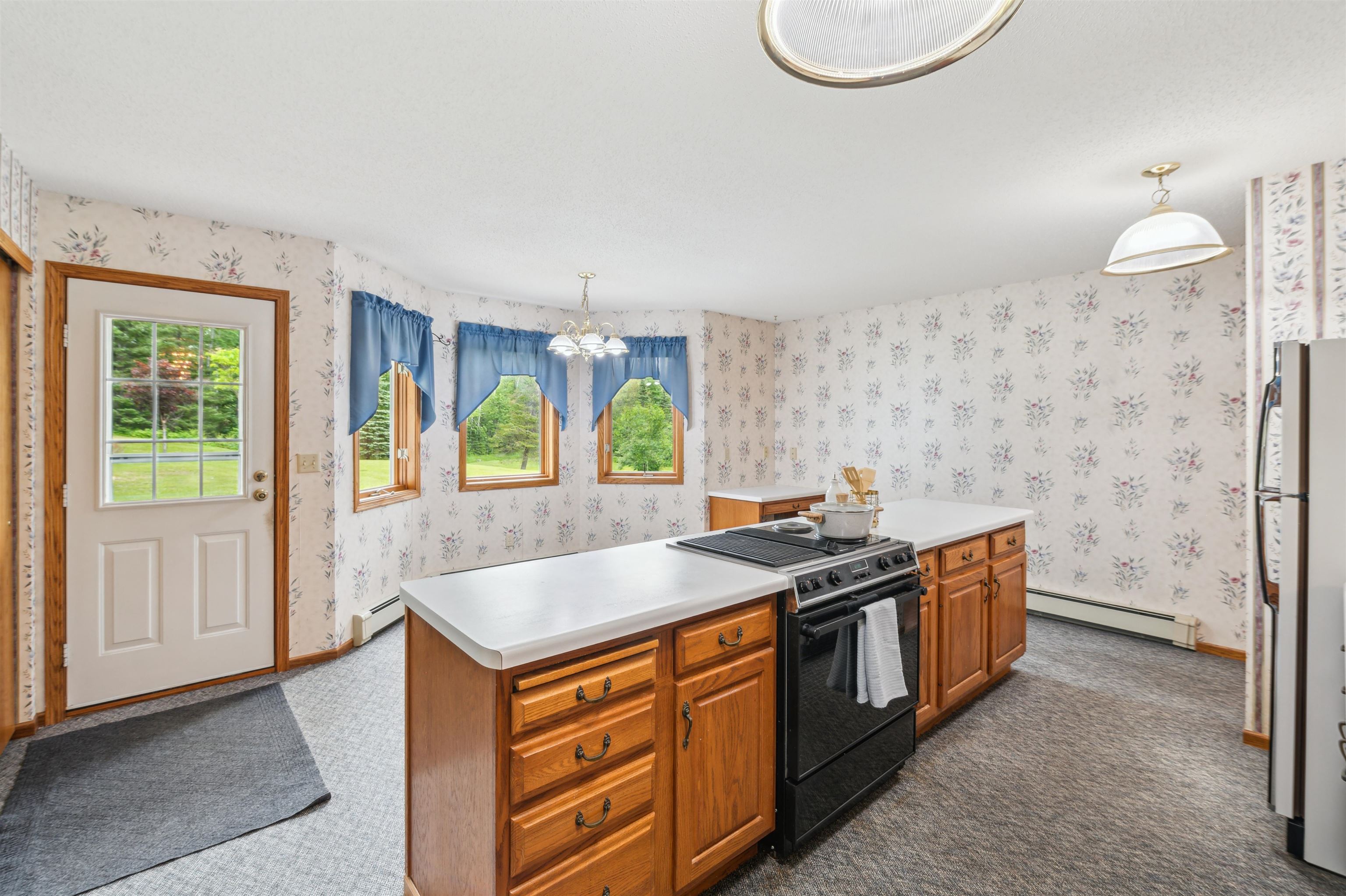 5948 Lavaque Road Duluth, MN 55803 - Photo 7 of 22 Kitchen with electric range, a baseboard heating unit, wallpapered walls, a chandelier, and dark carpet