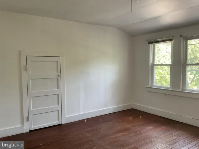 an empty room with wooden floor closet and windows