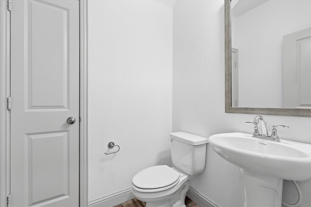 6141 Roper Road McKinney, TX 75070 - Photo 28 of 35 Pedestal sink with chrome faucet and framed mirror, complemented by a white toilet, paneled door, and wood-finish flooring