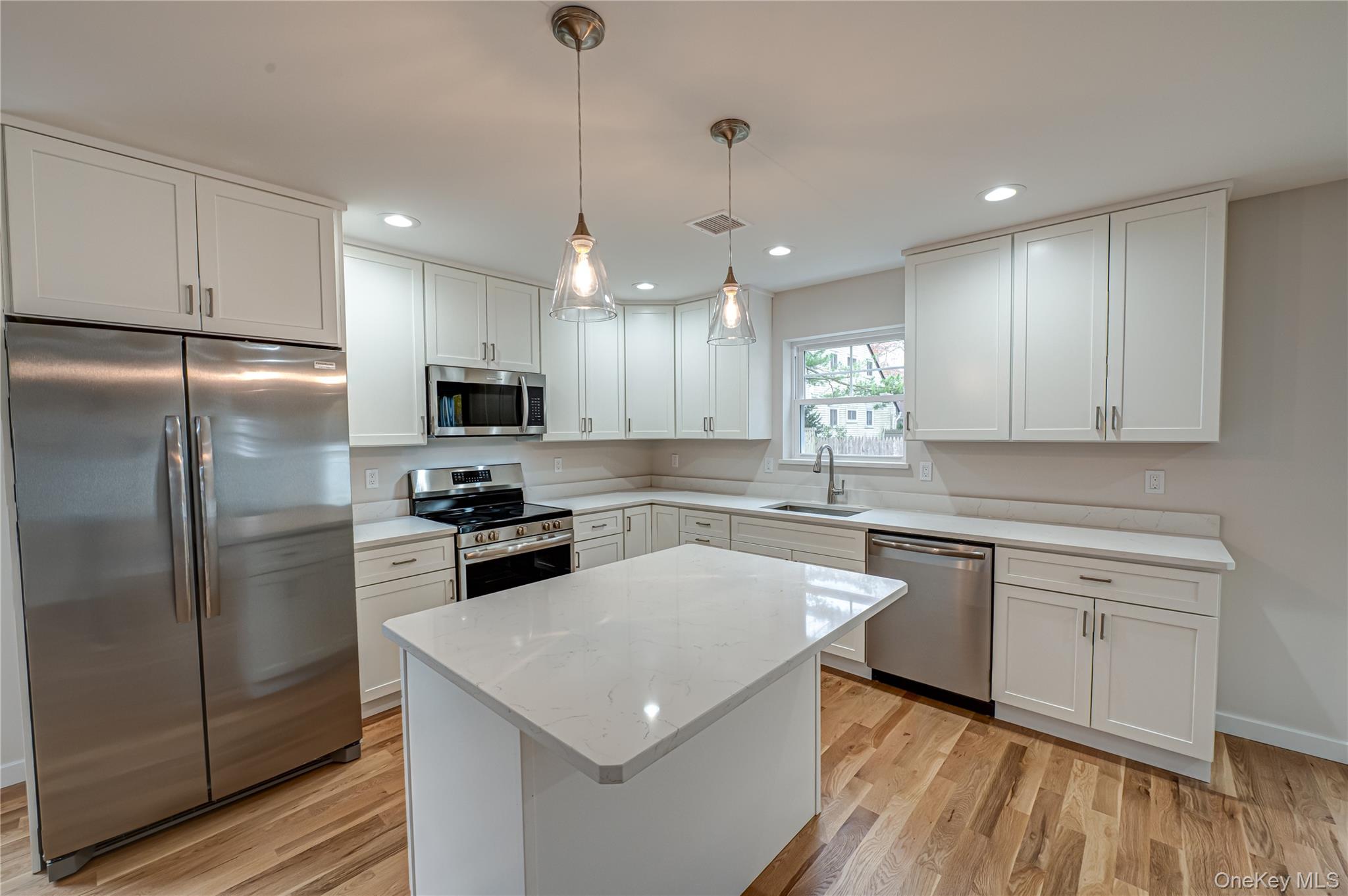Kitchen featuring stainless steel appliances, white cabinets, pendant lighting, light wood-type flooring, and recessed lighting