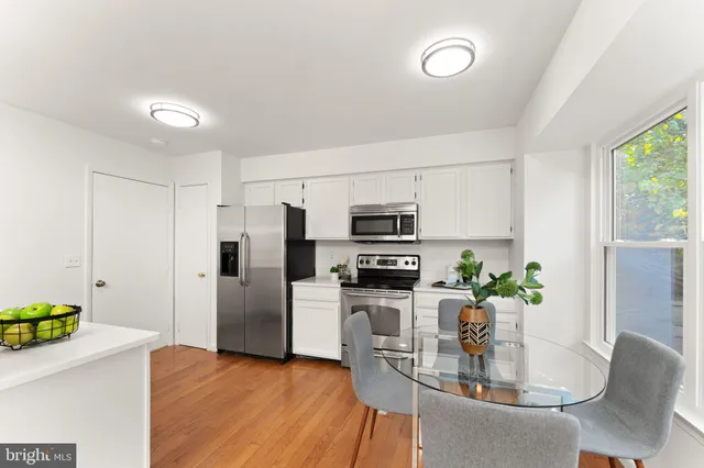 a kitchen with stainless steel appliances kitchen island granite countertop a refrigerator a stove a microwave a sink a dining table and chairs with wooden floor
