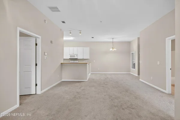 a view of an empty room with kitchen and window