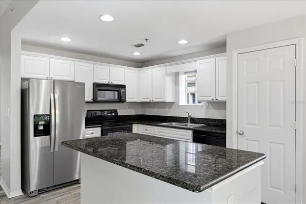 a kitchen with stainless steel appliances granite countertop a refrigerator a stove a sink a microwave and white cabinets