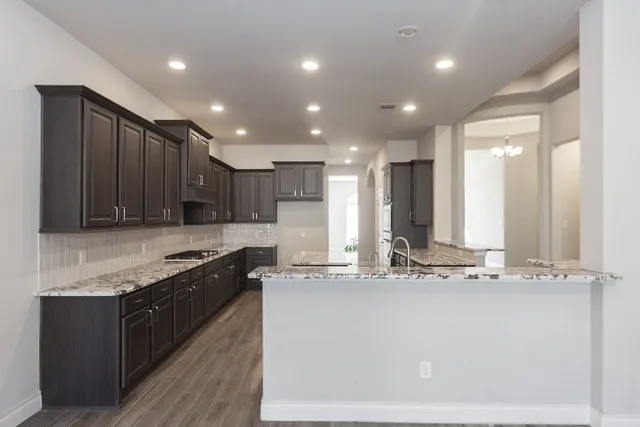 a view of an empty room with wooden floor and a kitchen