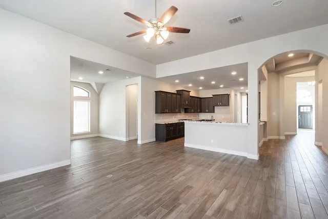 a view of an empty room and kitchen with wooden floor